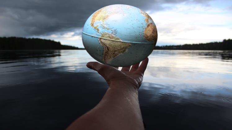 A hand holds a globe over a lake.